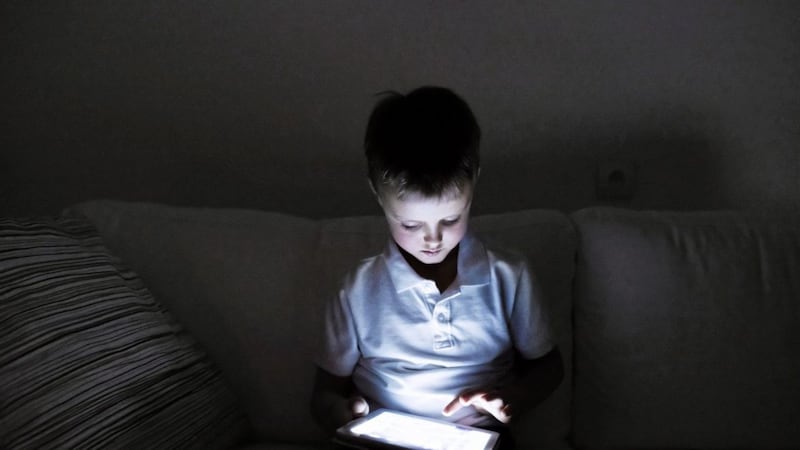 Little boy playing with tablet, sitting on sofa in dark room at night. 