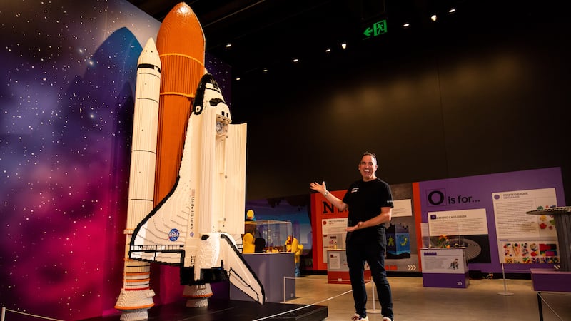 Ryan 'The Brickman' Naught poses beside a model of a US Space Shuttle, just one of his many creations from Bricktionary: The Interactive Lego Brick Exhibition