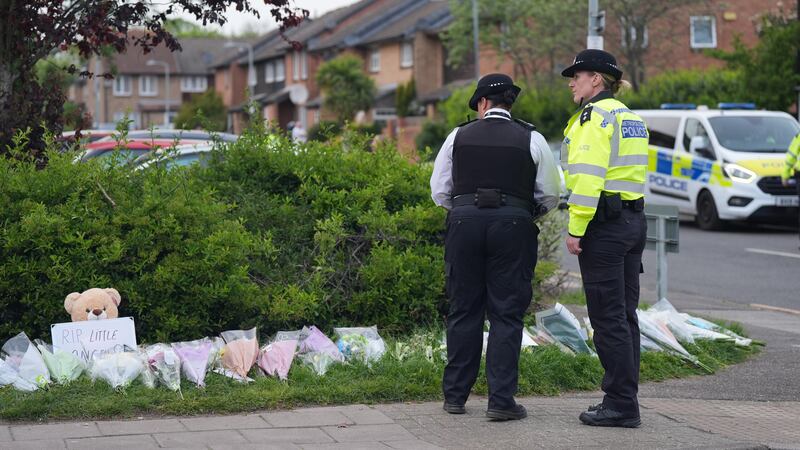 Police officers look at flowers laid at the scene of the incident in Hainault