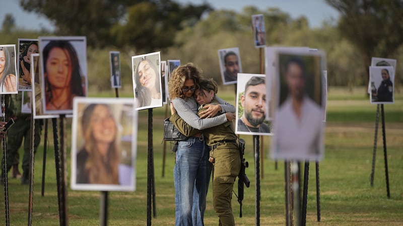 Israelis embrace next to photos of people killed and taken captive by Hamas militants (Ohad Zwigenberg/AP)