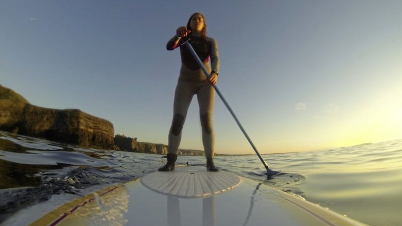 Paddle boarder Jennifer Greenlees on the north Antrim coast, Dunluce in the background 