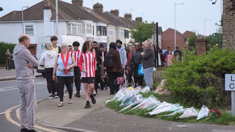 Members of the community looking at floral tributes in Hainault, north east London