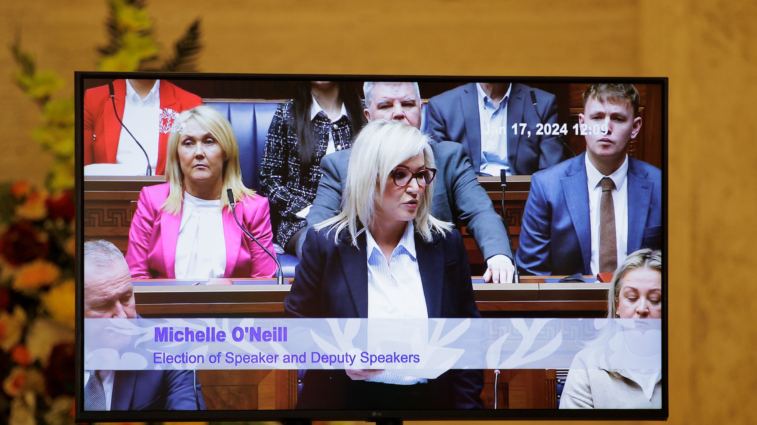 A television screen displays a live feed from the Assembly chamber as Sinn Fein Vice President Michelle O'Neill addresses fellow politicians