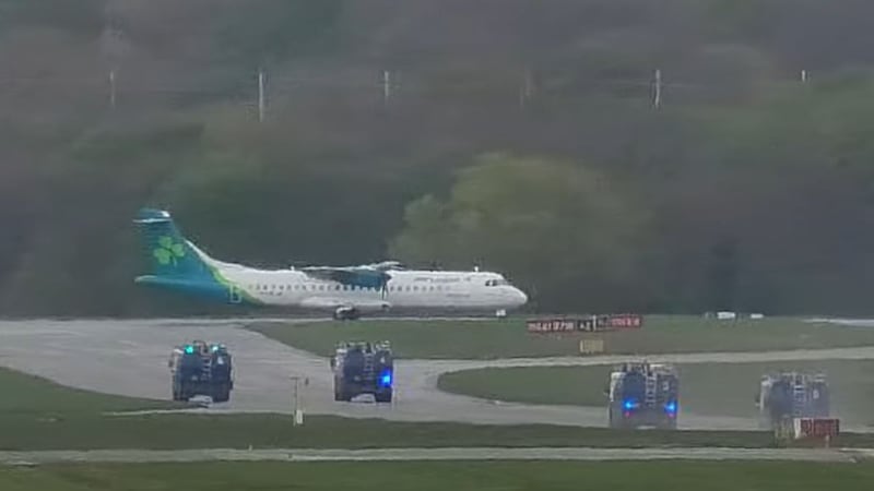 An Air Lingus aeroplane taxis along a runway while police vehicles with flashing blue lights are parked nearby