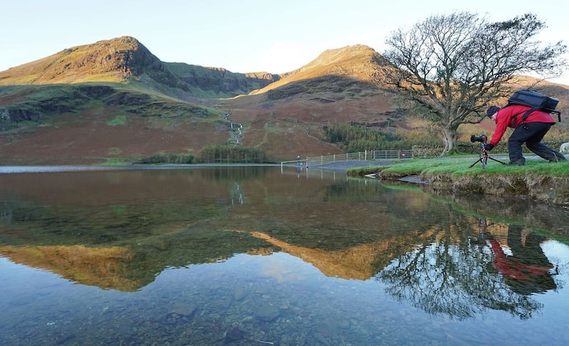 A photographer lines up his shot of autumn reflections in lake Buttermere in the Lake District, Cumbria