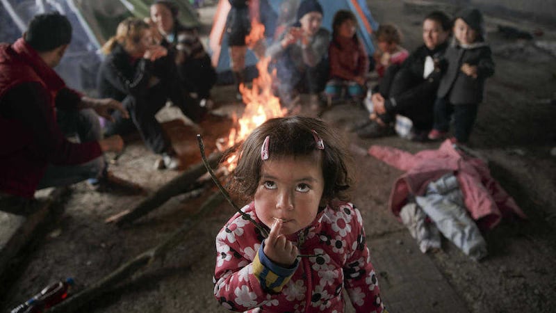 A migrant child eats as others sit around a fire in a railway repairs hangar where people have set up their tents at the northern Greek border point of Idomeni, Greece. Picture by Vadim Ghirda, Associated Press
