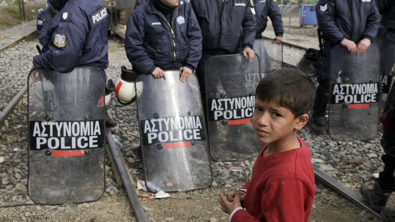A boy stands near a line of Greek policemen as migrants block a railway during a protest demanding the opening of the border between Greece and Macedonia in the northern Greek border station of Idomeni. Picture by Association Press