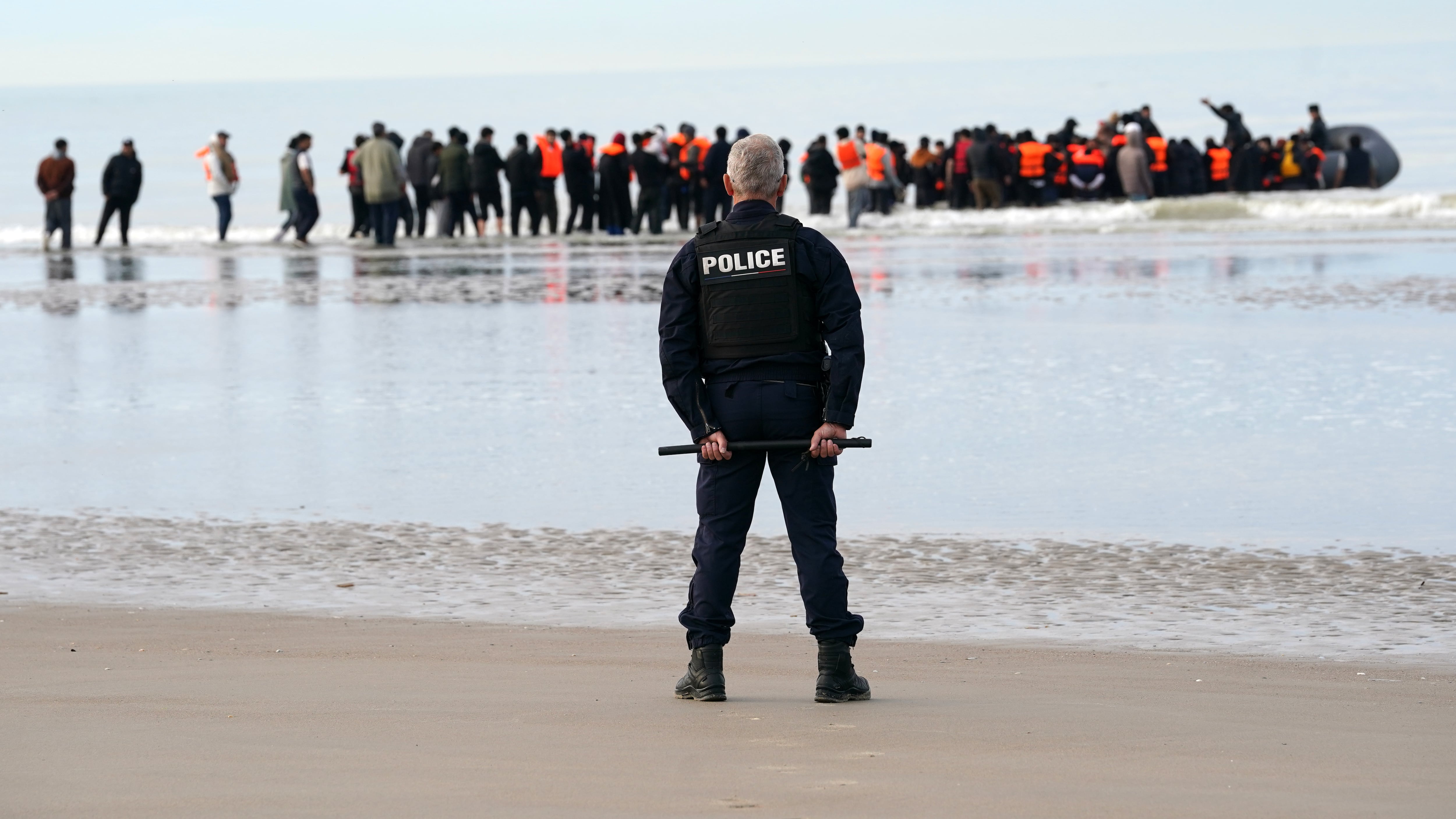 A police officer watching people thought to be migrants boarding a small boat in Gravelines, France