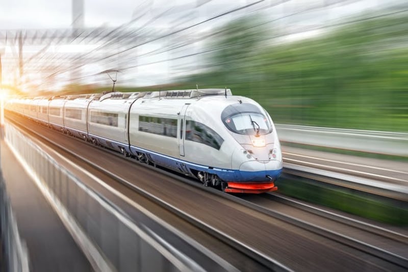 Modern high-speed train driving past a station in a city.