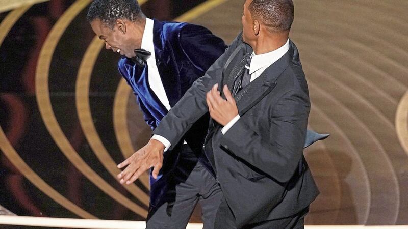 Will Smith, right, hits presenter Chris Rock on stage while presenting the award for best documentary feature at the Oscars on Sunday, March 27, 2022, at the Dolby Theatre in Los Angeles. (AP Photo/Chris Pizzello). 