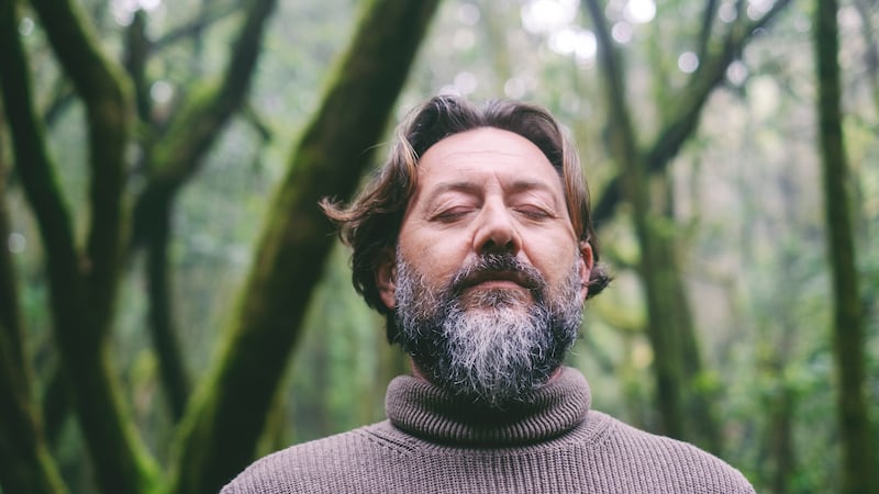 Front portrait of mature man with beard and closed eyes in outdoor leisure activity alone. Male people in meditation with green nature background. Environment and alternative adventure journey