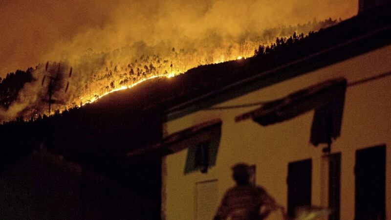 A man on the balcony of a house looks up at a forest fire raging on a hillside above the village of Avelar, central Portugal, before sunrise Sunday PICTURE: Armando Franca 