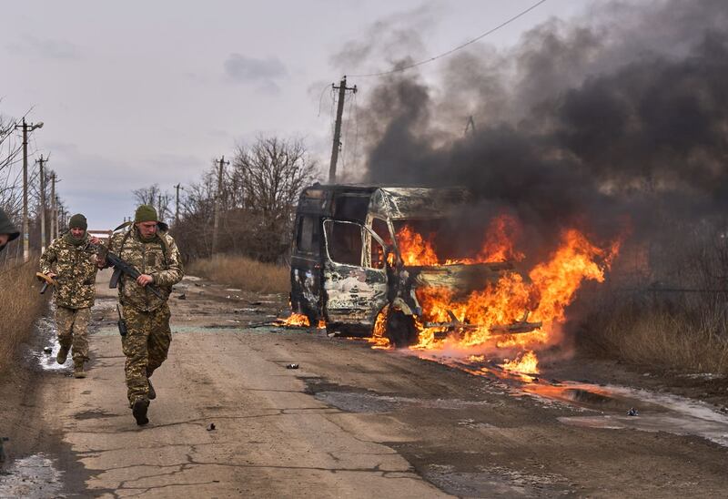 Ukrainian soldiers pass by a burning volunteer bus