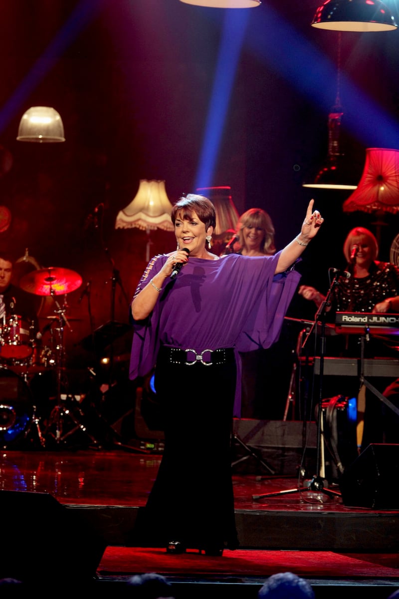 Susan McCann, glamorously dressed in purple, happy performing on stage