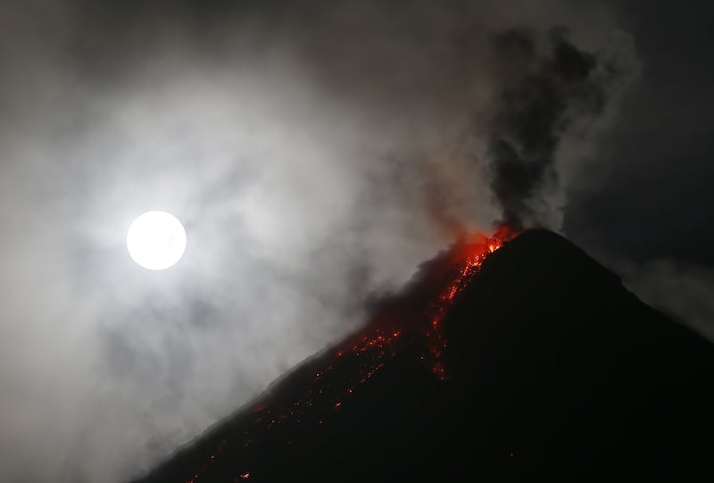 A bright white moon shines above erupting volcano