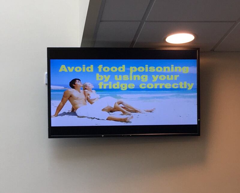 TV screen showing a white couple on a sundrenched white beach with the text "avoid food poisoning by using y our fridge correctly"