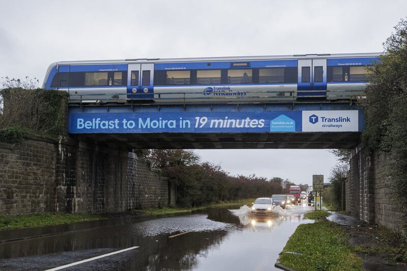 A car drives through a flooded area under a railway bridge as a train passes overhead, on the A26 outside the village of Moira in Northern Ireland (Liam McBurney/PA)