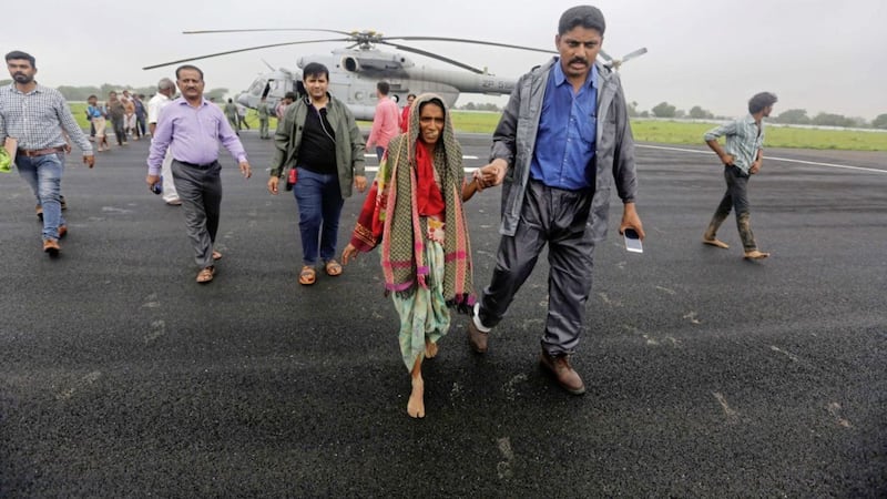 An Indian man escorts a woman who was air lifted from a flooded farm after she arrived at an airport in Deesa, Gujarat, India Picture: Ajit Solanki/AP 