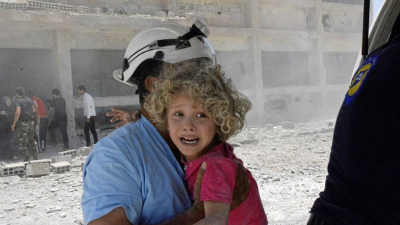 A civil defense worker carrying a child after airstrikes hit a school housing a number of displaced people in the western part of the southern Daraa province of Syria. Picture by Syrian Civil Defense White Helmets via Associated Press 