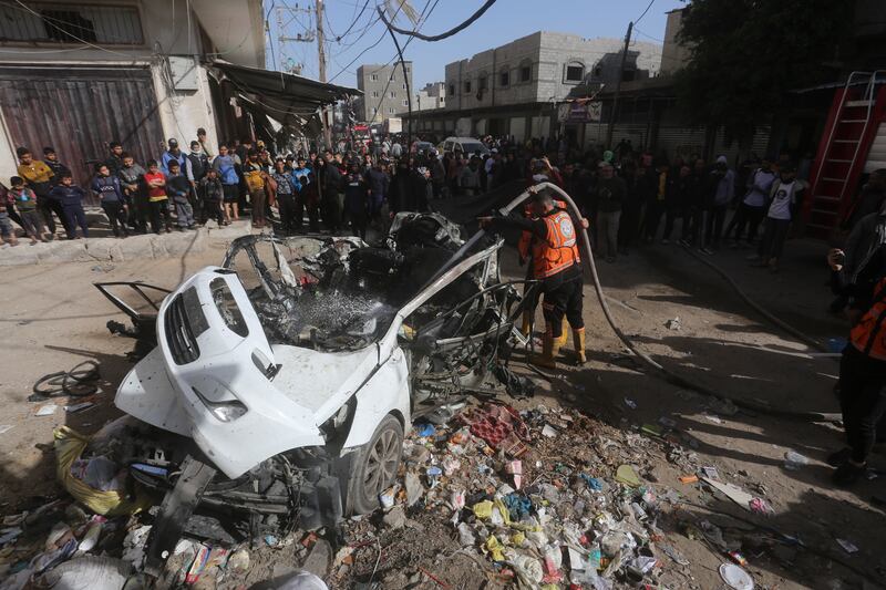 Palestinians stand around a car targeted in an Israeli air strike in Rafah (AP Photo/Hatem Ali)