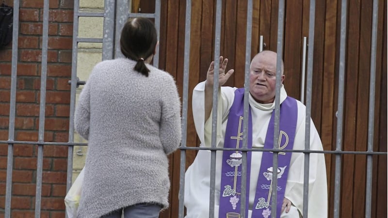Fr Paddy McCafferty hears confessions while observing social distancing guidelines though the locked gates of Corpus Christi Church in Ballymurphy, west Belfast. Picture by Hugh Russell 