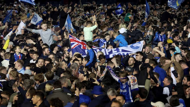 Portsmouth fans celebrate on the pitch after their team secured promotion