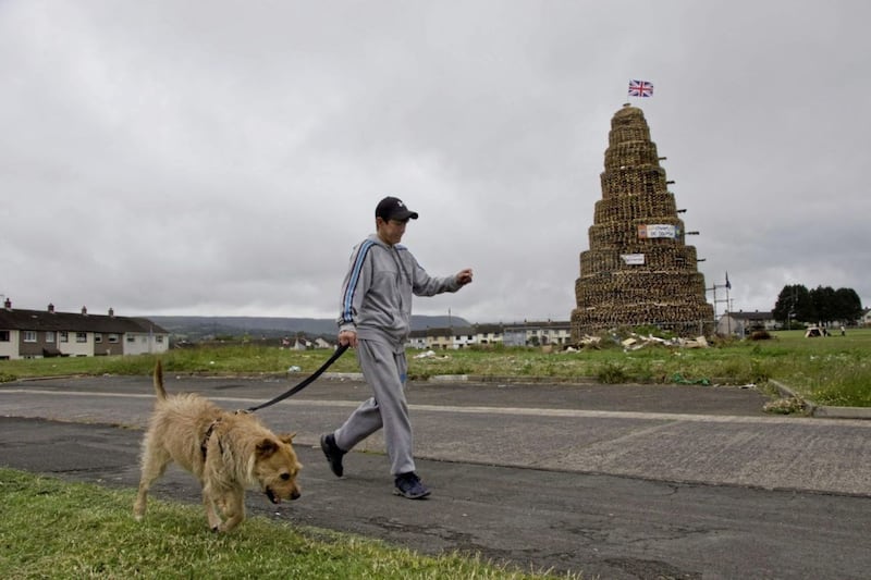 A dog-walker strides out past a towering bonfire waiting to be lit 