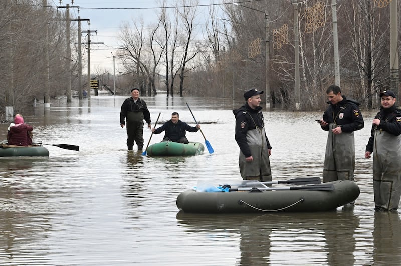Police officers guard an area as people use rubber boats in a flooded street after part of a dam burst, in Orsk, Russia (Anatoly Zhdanov/Kommersant Publishing House via AP)
