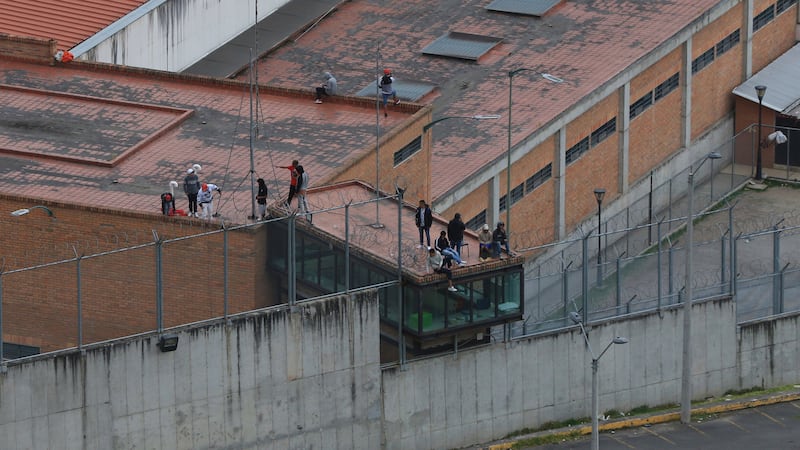 Prisoners stand on the roof of the Turi jail where dozens of prison guards and police officers have been kidnapped by the inmates (AP)