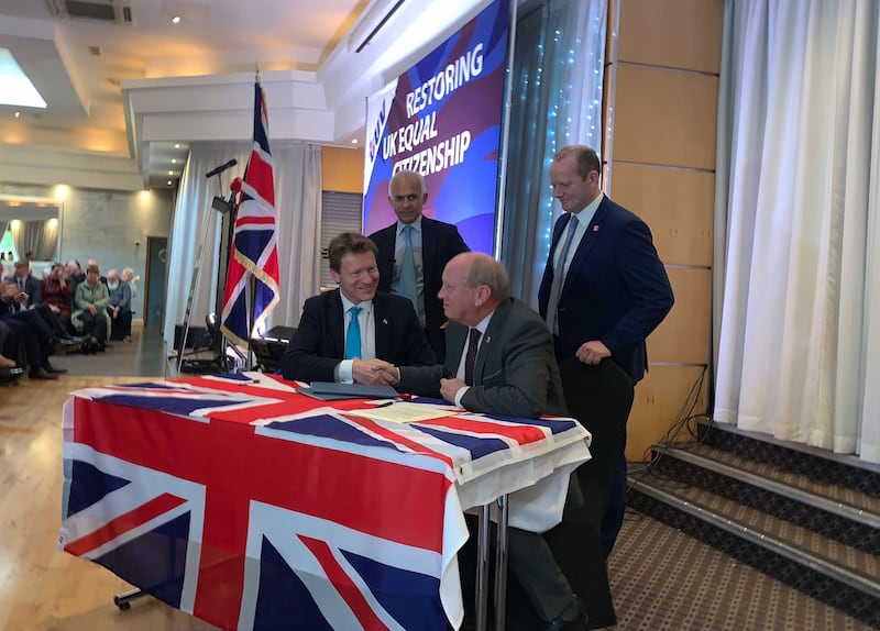Reform UK leader Richard Tice and TUV leader Jim Allister shake hands, seated at a table covered in a union flag