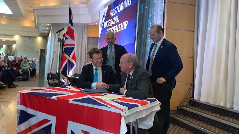 Reform UK leader Richard Tice and TUV leader Jim Allister shake hands, seated at a table covered in a union flag