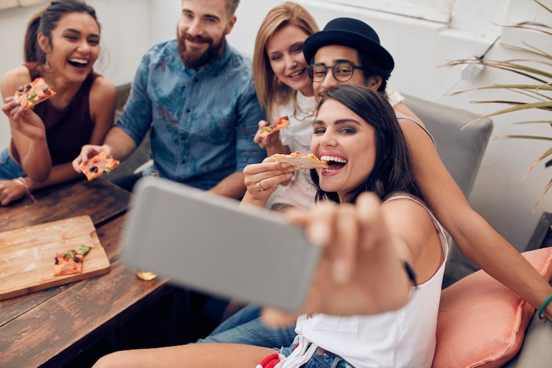 Young people taking a selfie while eating pizza.