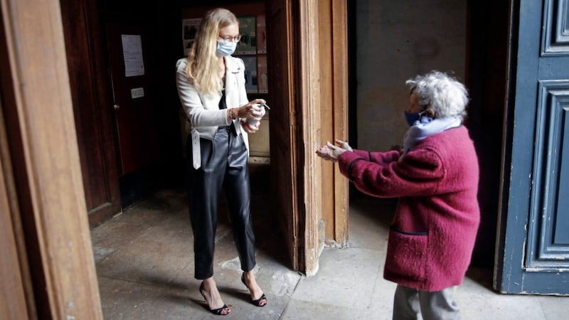 A woman offers hand gel to a worshipper before entering Saint Roch church in Paris last weekend. Picture by Francois Mori, AP Photo