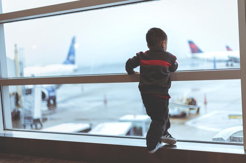 Child looking at planes through the window at the airport.