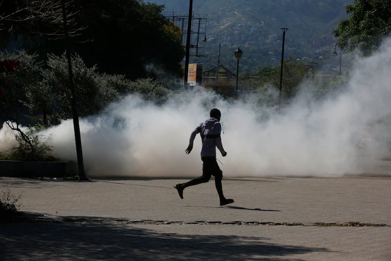 A man runs for cover as riot police launch tear gas in an effort to remove street vendors in the Champs de Mars area, next to the National Palace, in Port-au-Prince, Haiti (Odelyn Joseph/AP)
