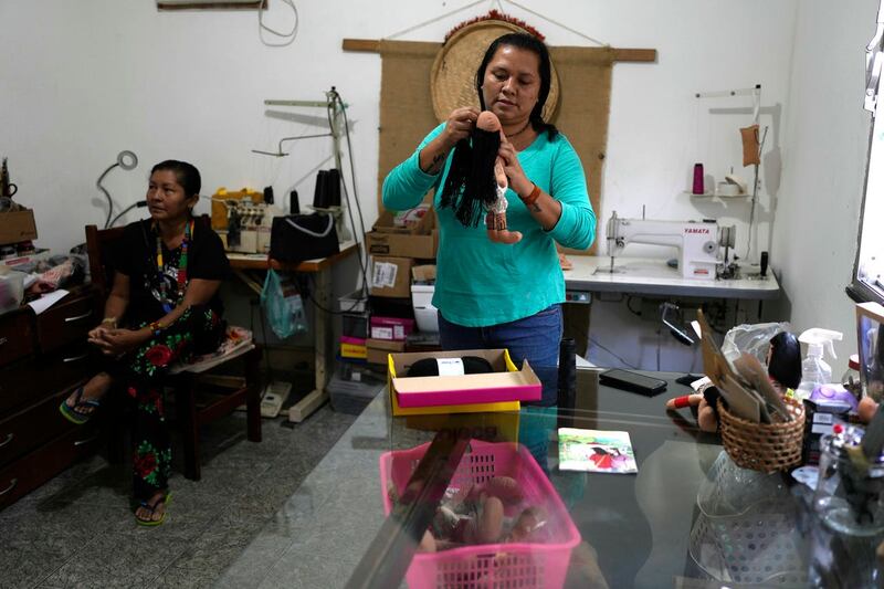 Atyna Pora, of Brazil’s Anambe indigenous group, adds black yarn hair to an indigenous doll, at the sewing workshop in her home in Rio de Janeiro, Brazil