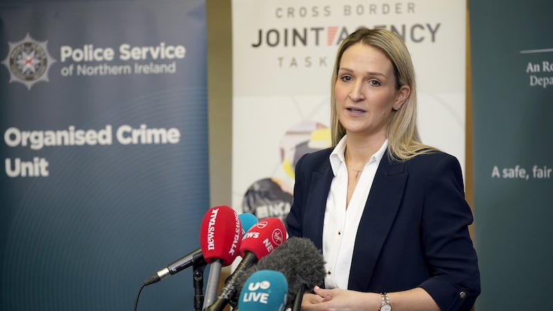 Irish Minister for Justice Helen McEntee speaking at the 2024 Cross Border Police Conference on Organised & Serious Crime, wearing a navy blue blazer and a white shirt with various media microphones in front of her
