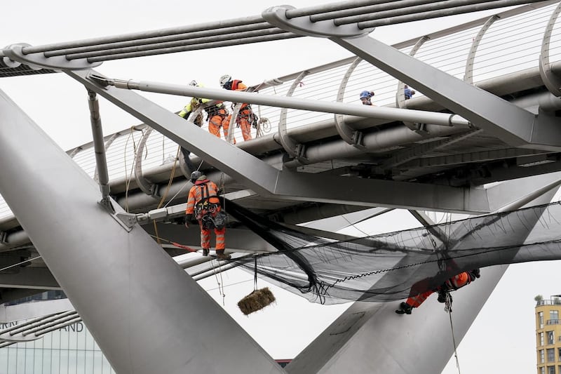A straw bale is suspended from London’s Millennium Bridge as work is undertaken on the structure