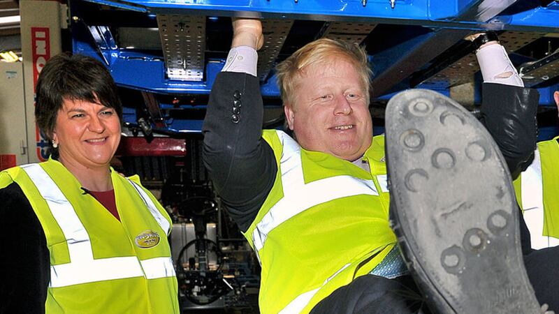 Boris Johnson doing pull-ups on the chassis of a Routemaster bus during a visit to Wrightbus in Antrim as Arlene Foster looks on&nbsp;