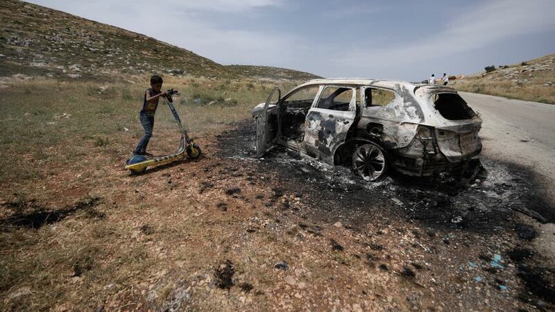 A Palestinian child inspects a burned car, which farmers say was set on fire by Israeli settlers, in the village of al-Mughayyir near the West Bank city of Ramallah (Majdi Mohammed/AP/PA)