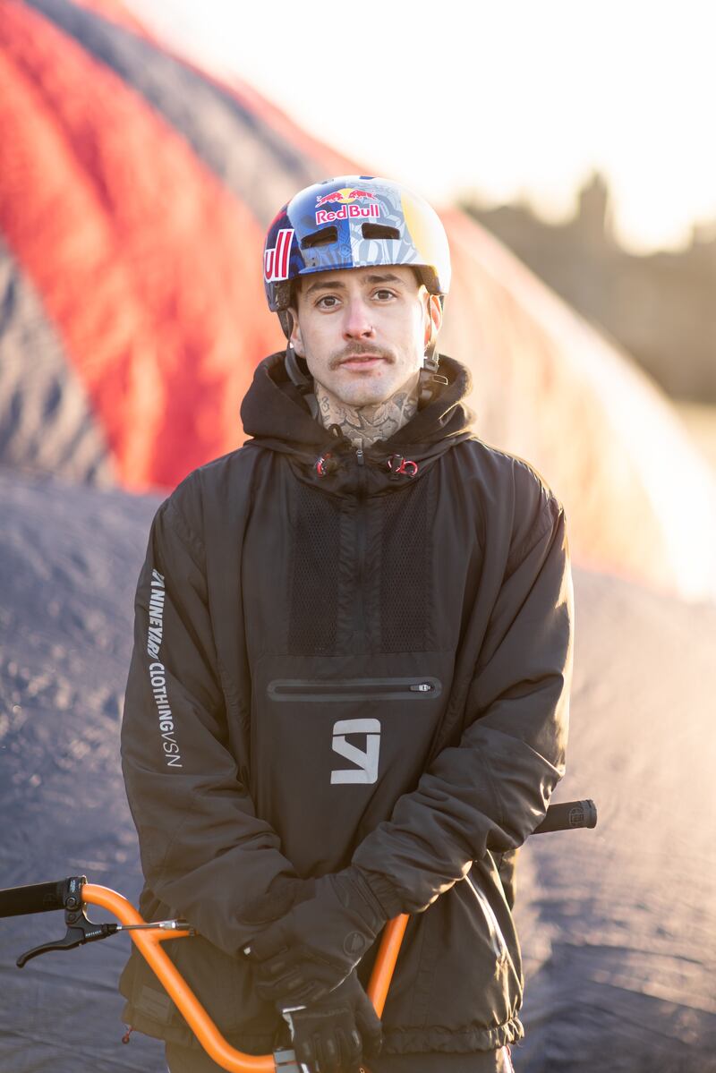 BMX athlete Kriss Kyle, sat on his bike and wearing a helmet, stood in front of a large hot air balloon