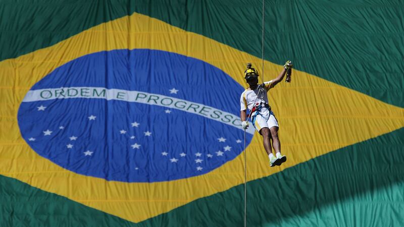<span style="font-family: Arial, Verdana, sans-serif; ">Brazilian athlete Hudson Alves rappels down in front of a huge Brazilian flag, carrying the Olympic flame in a lantern during the torch relay in Brasilia on Tuesday</span>